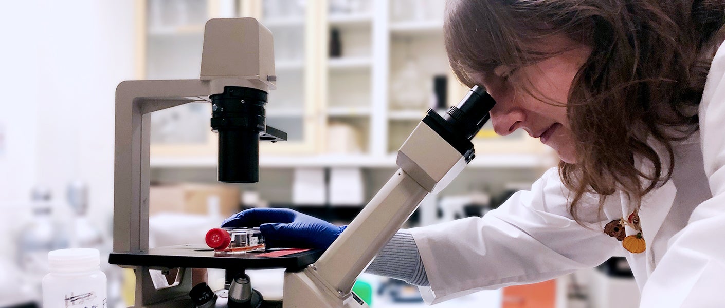 A woman looks through a microscope while adjusting a specimen on the stage